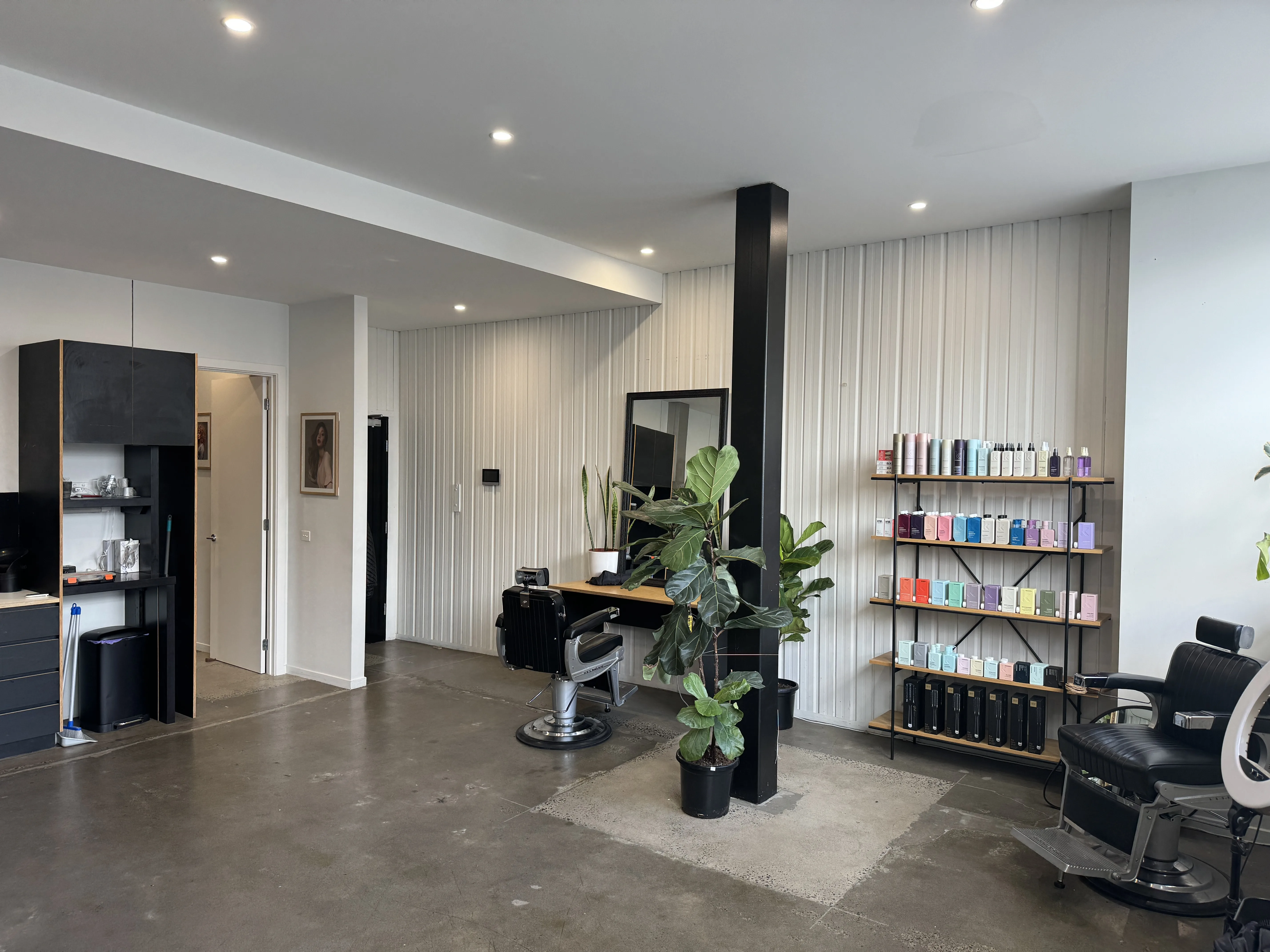 Salon interior — vintage barber chair at a plywood station, Kevin Murphy product wall, black steel column