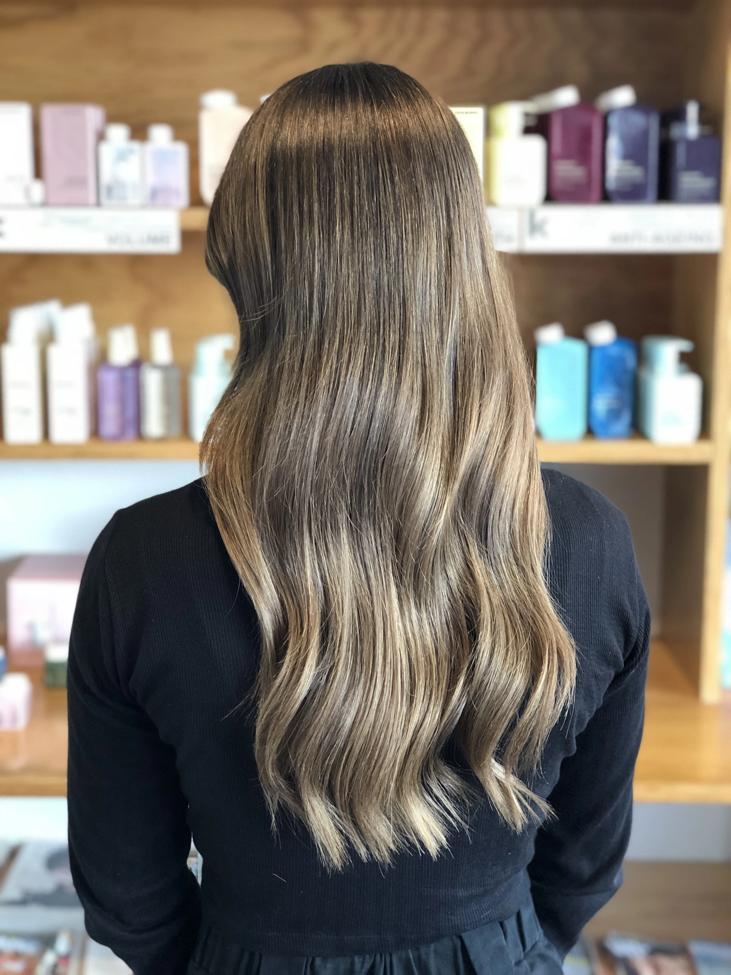 In-salon client result — back of head, long brunette-to-blonde balayage waves