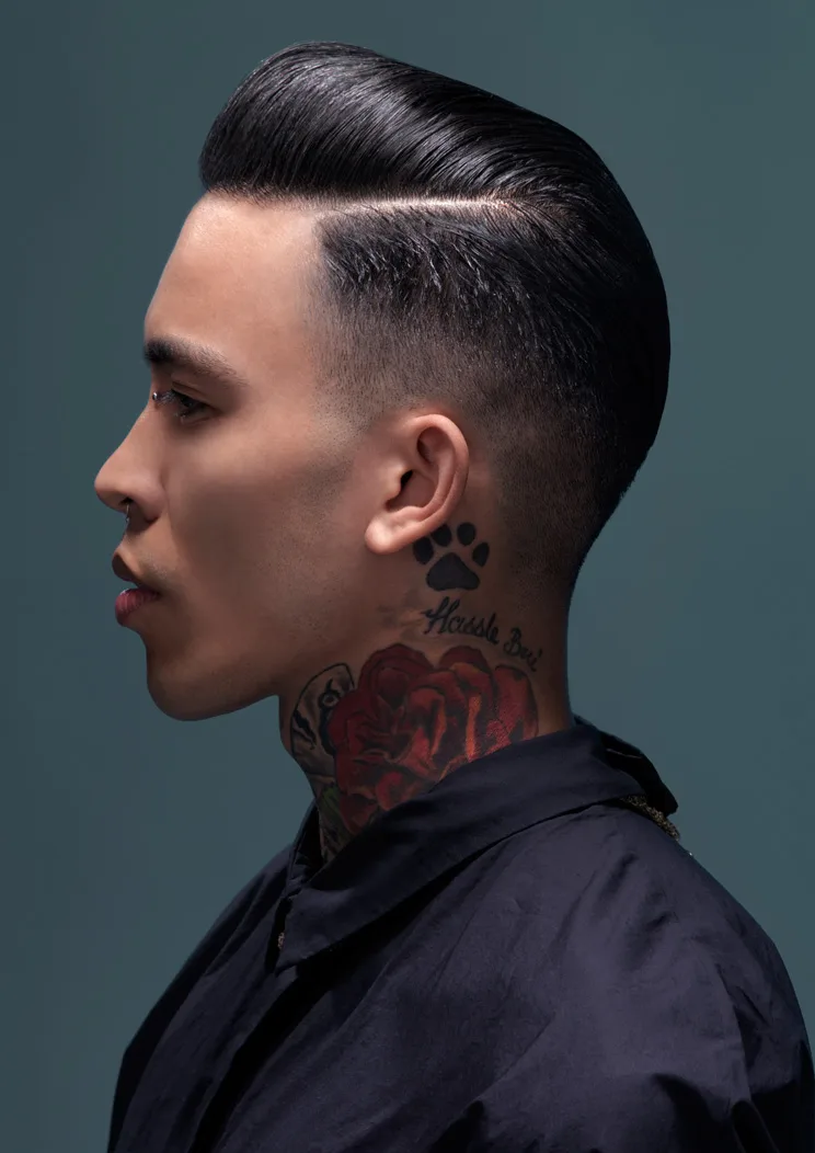 Editorial — man in side profile, sleek dark pompadour with neck tattoos, teal backdrop