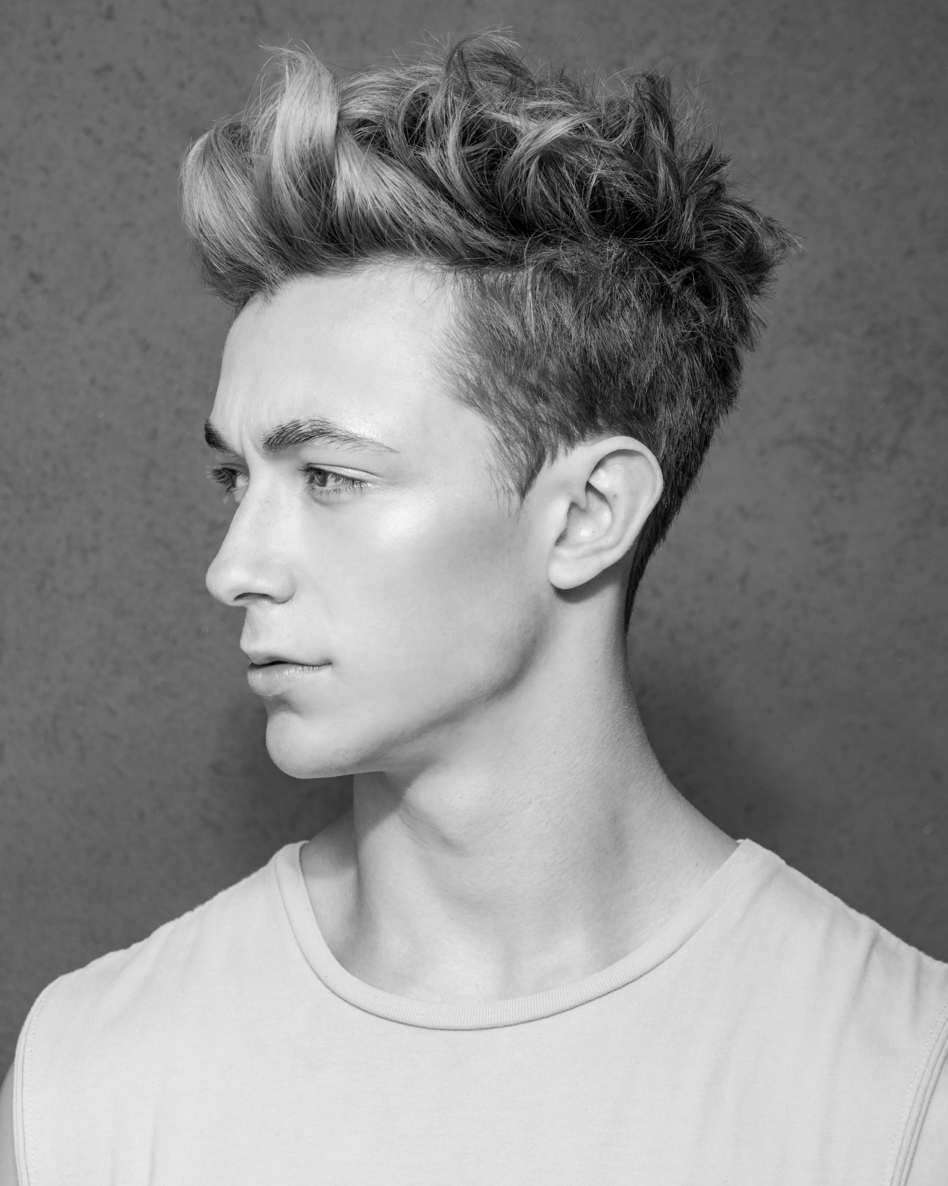 Editorial B&W — young man in profile, textured tousled quiff against grey studio backdrop