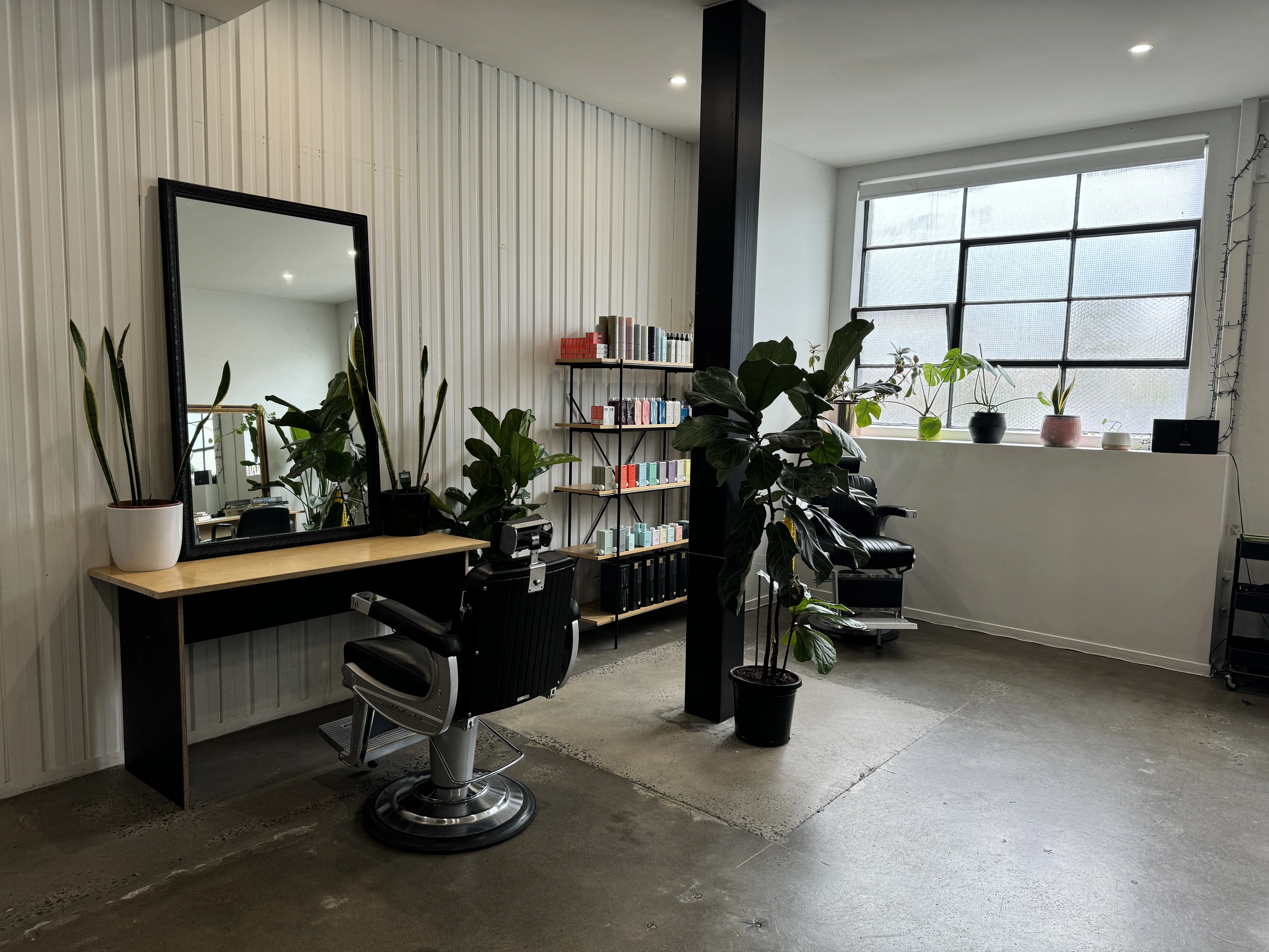 Ziyad Salon styling station — black-framed mirror on plywood desk, barber chair and industrial window