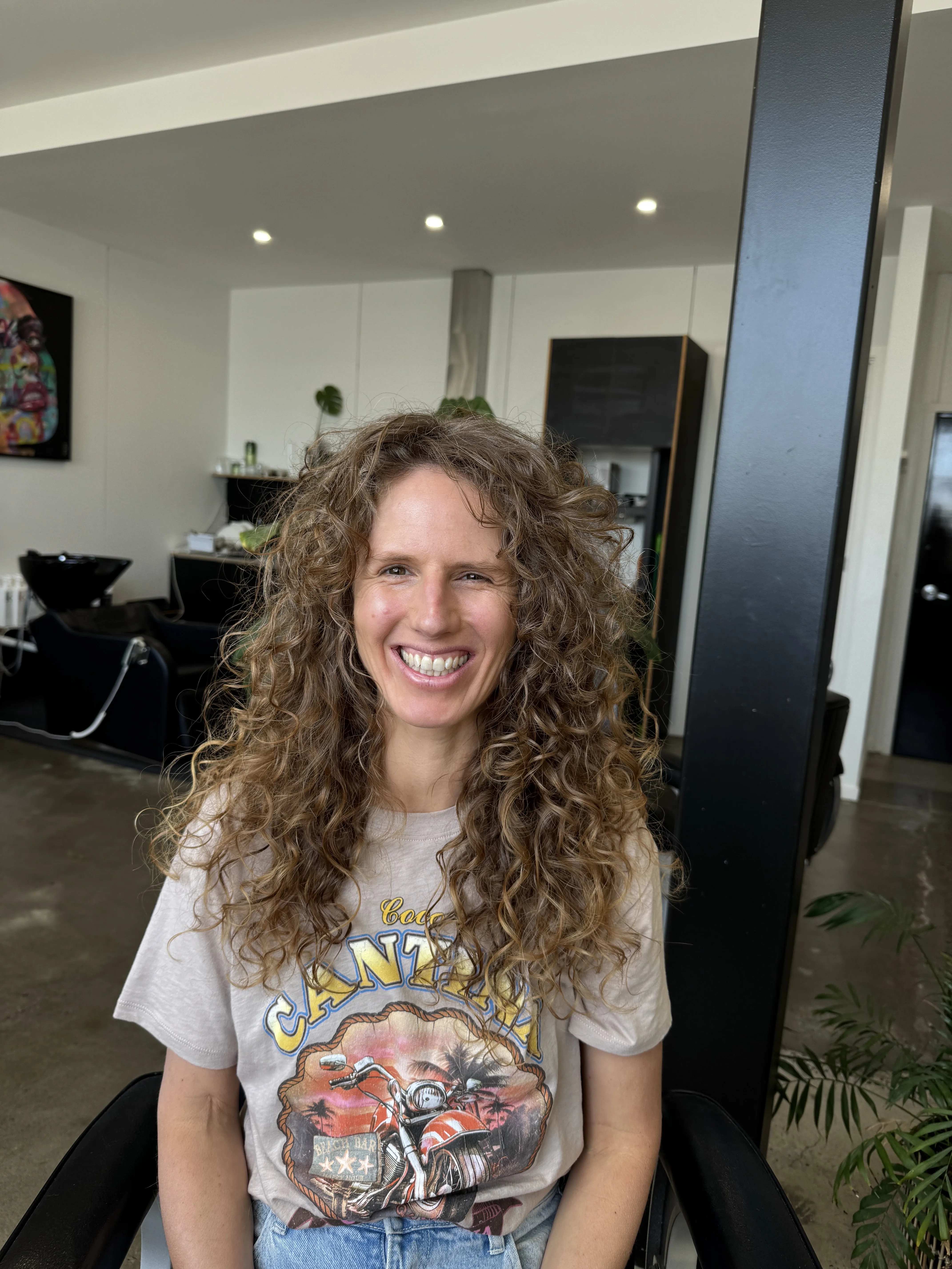 In-salon client — woman, long natural brown curls, in-salon with wash basin behind