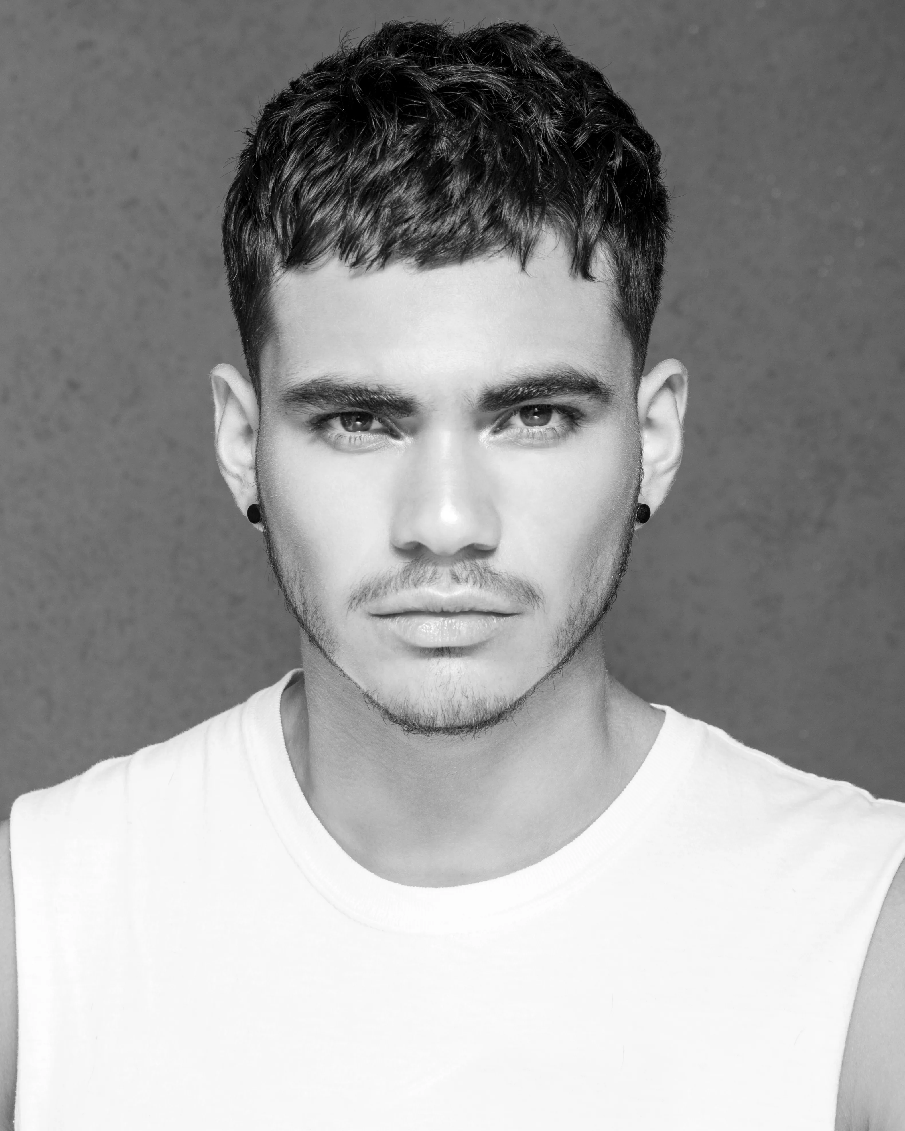 Editorial B&W — man, short curly textured crop, white tank, grey wall